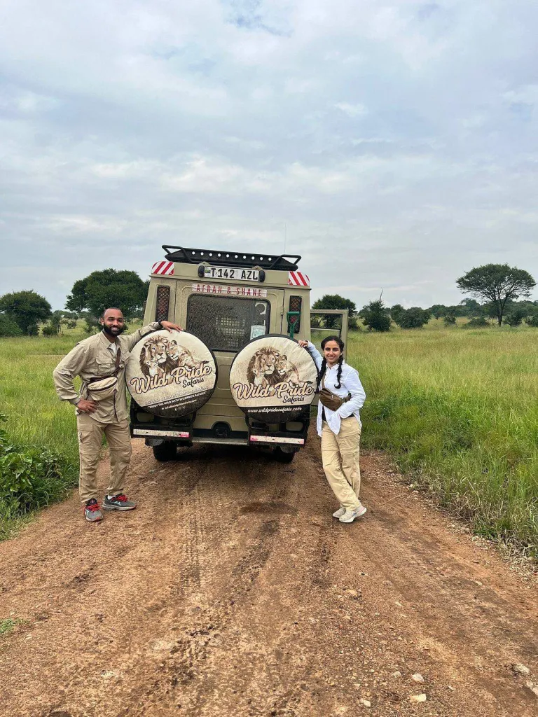 Two travellers beside a Wild Pride Safaris Land Cruiser on a dirt track